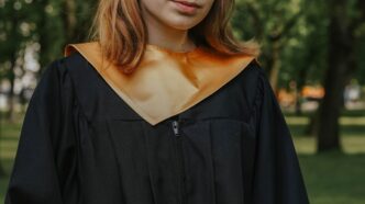 Absolventin mit Talar und Hut haelt eine Urkunde in der Hand