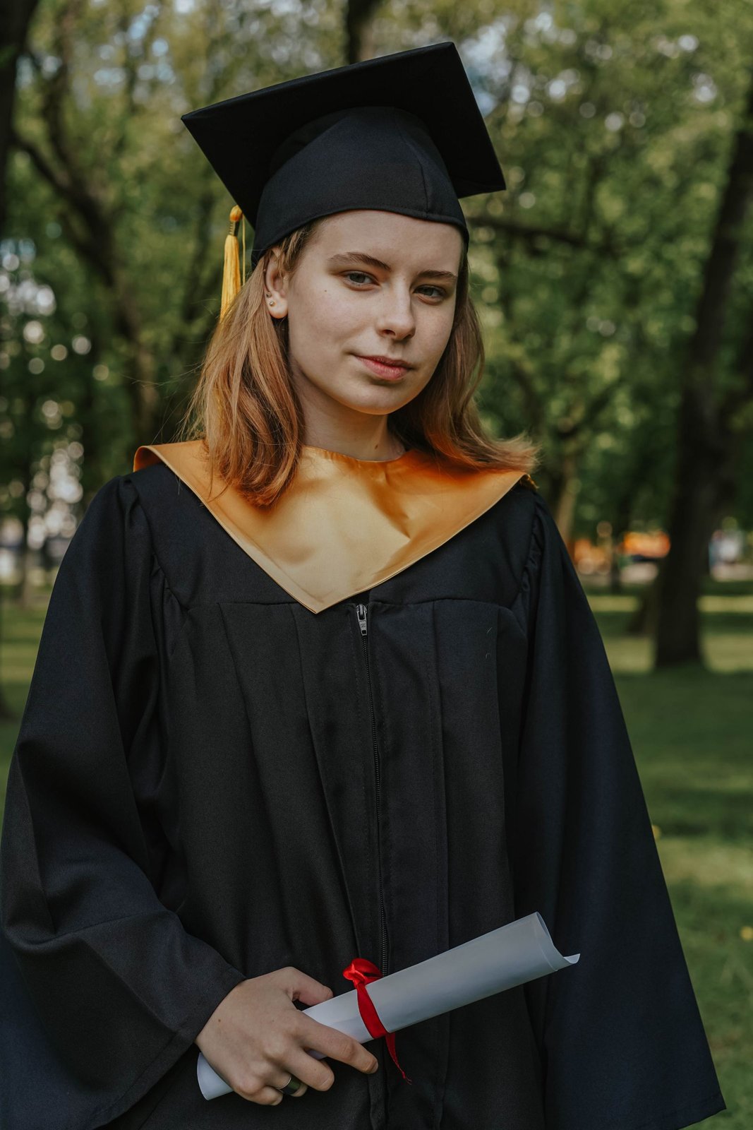 Absolventin mit Talar und Hut haelt eine Urkunde in der Hand
