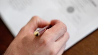 Person unterschreibt einen Gesellschaftsvertrag mit Kugelschreiber an einem Holztisch