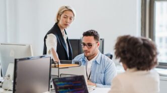 Drei Personen besprechen am Schreibtisch im Büro gemeinsam Unterlagen am Laptop
