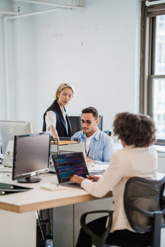 Drei Personen besprechen am Schreibtisch im Büro gemeinsam Unterlagen am Laptop