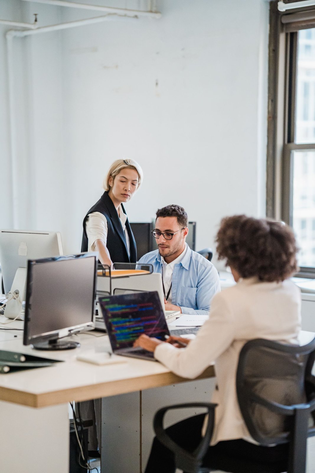 Drei Personen besprechen am Schreibtisch im Büro gemeinsam Unterlagen am Laptop