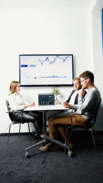Drei Personen sitzen im Buero an einem Tisch und besprechen Kennzahlen am Bildschirm