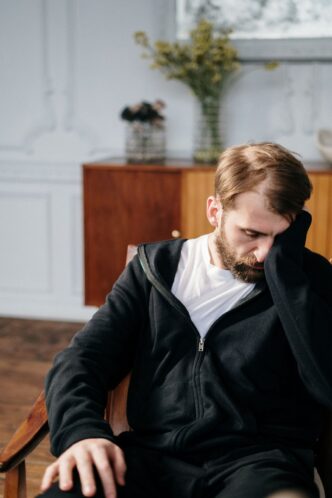Nachdenklicher Mann sitzt mit gesenktem Blick auf einem Stuhl
