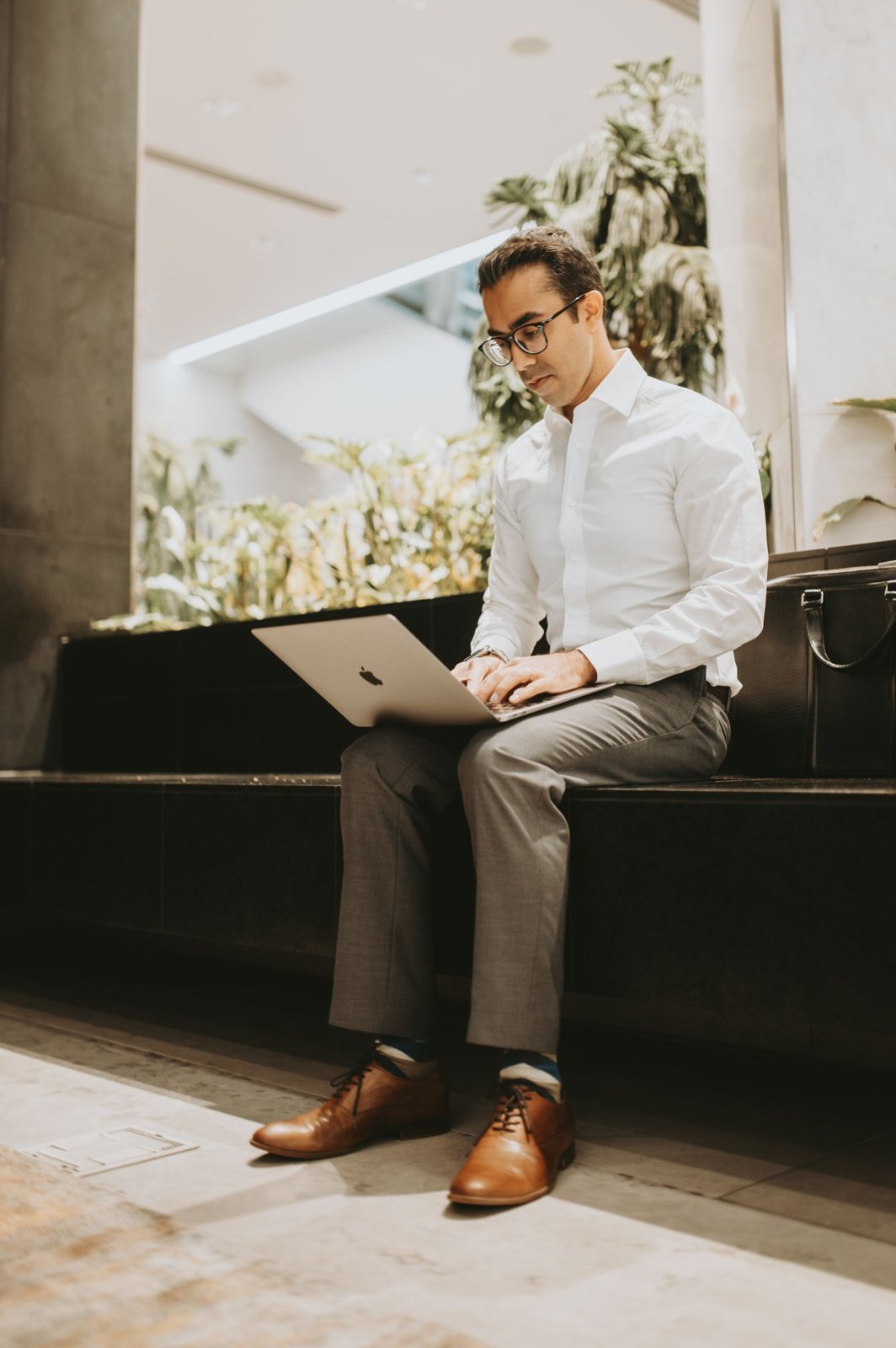 Mann im Hemd arbeitet mit dem Laptop auf dem Schoss in einer Buerolobby