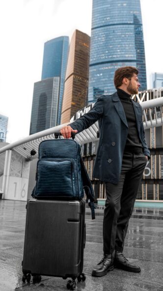 Mann mit Koffer und Rucksack steht vor einer Skyline und wartet auf die Abreise
