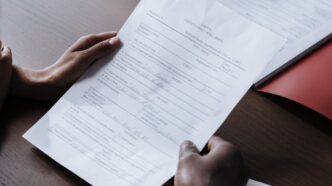 Zwei Personen reichen sich am Tisch ein ausgefuelltes Formular zur Unterschrift