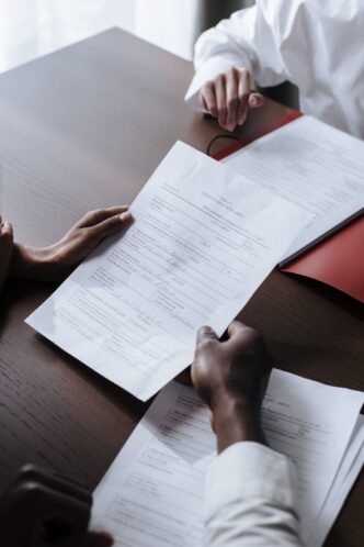 Zwei Personen reichen sich am Tisch ein ausgefuelltes Formular zur Unterschrift