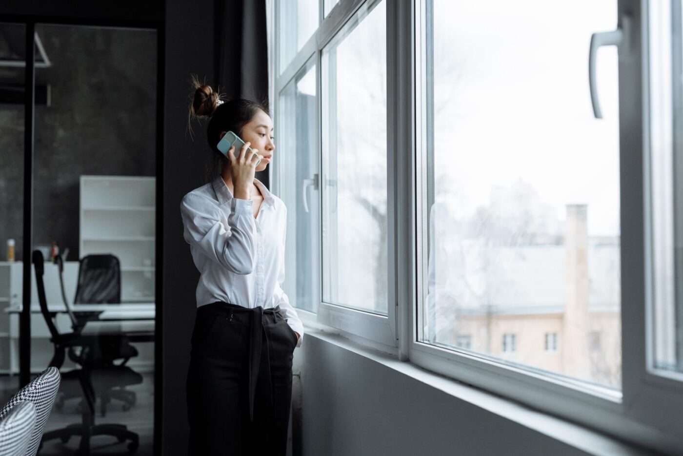 Frau telefoniert am Fenster eines hellen Bueros