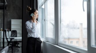 Frau telefoniert am Fenster eines hellen Bueros